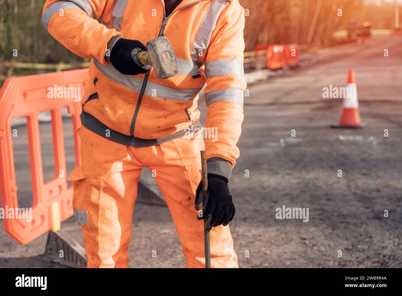 Le constructeur défonce la route en posant des goupilles en acier avec un marteau en morceaux pendant les travaux routiers. Constructeur martelant des barres d'acier dans l'asphalte pendant le roadwor Banque D'Images