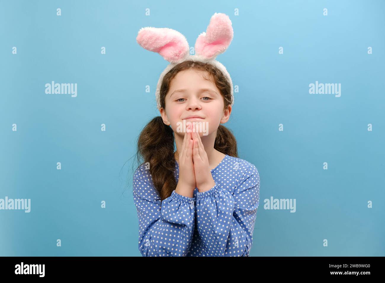 Portrait de jolie petite fille enfant portant des oreilles de lapin rose de pâques priant avec les mains ensemble demandant pardon souriant confiant, posant isola Banque D'Images