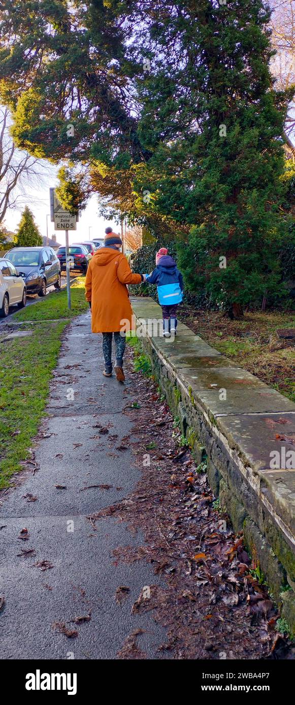 mère tient la main de son fils alors qu'il marche sur un mur sur le côté du trottoir Banque D'Images