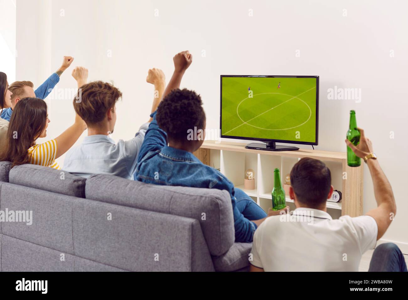 Groupe d'amis divers assis sur le canapé, boire de la bière et regarder le football à la télévision Banque D'Images