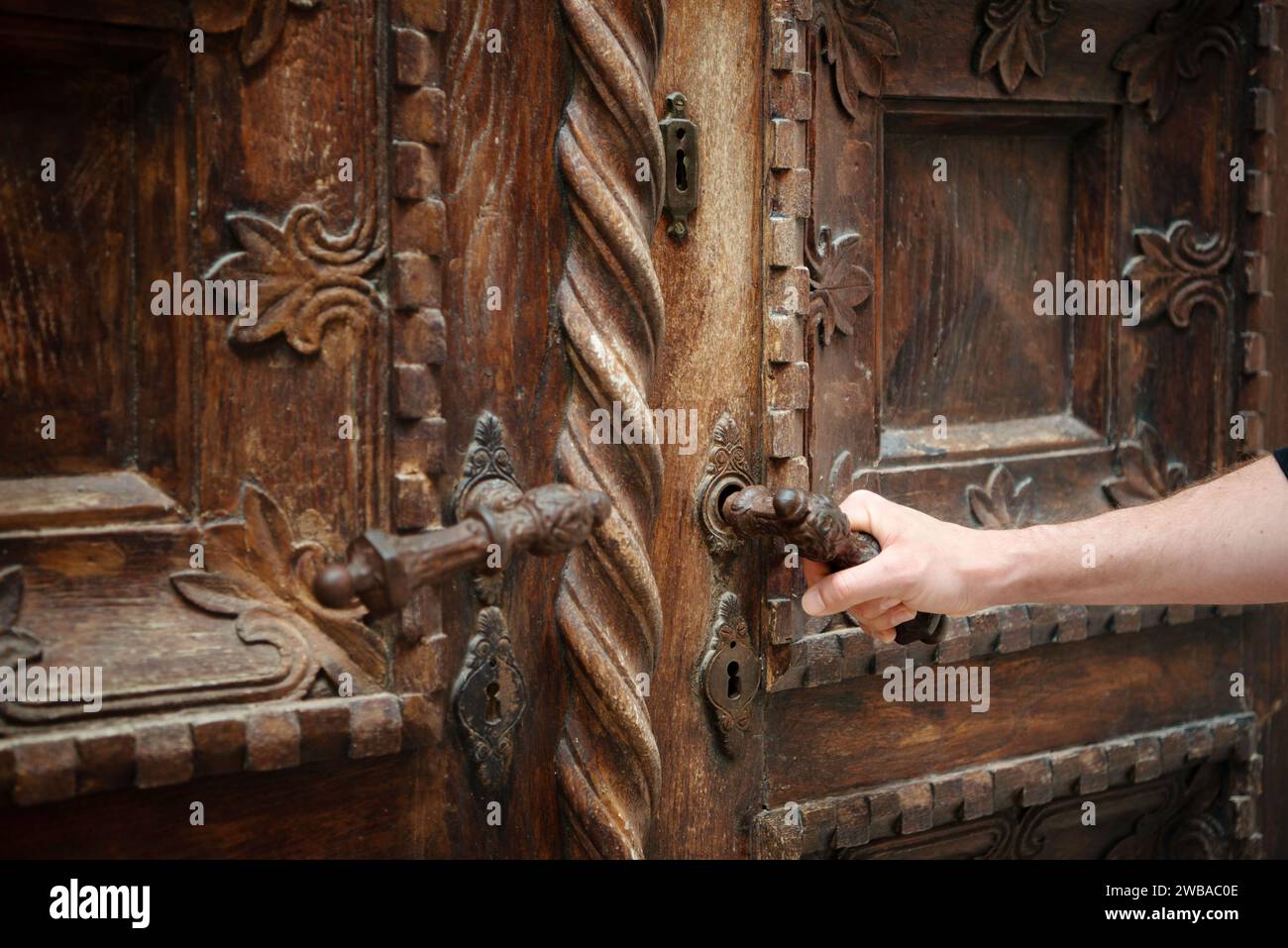 Main ouvrant une porte sculptée ornée et magnifiquement en bois. Banque D'Images