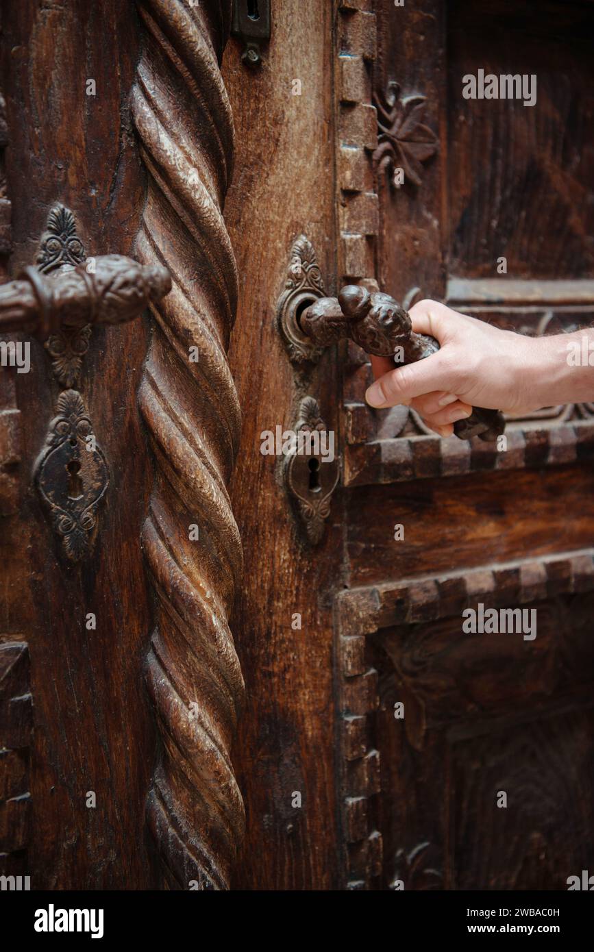 Mans Hand ouvre une porte sculptée ornée et magnifiquement en bois qui ouvre sur une église. Banque D'Images