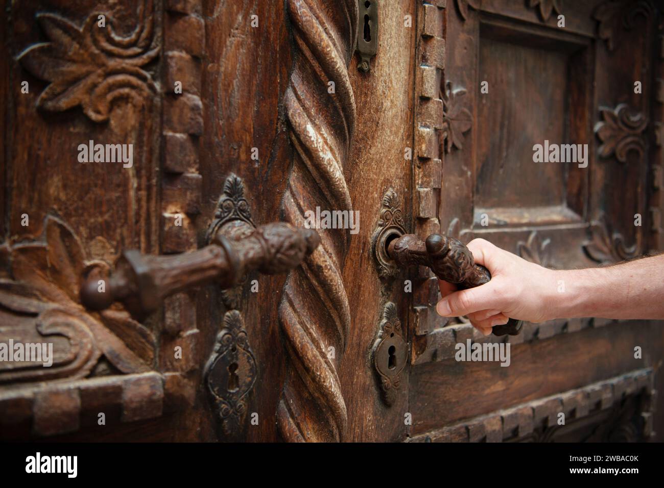 Main ouvrant une porte sculptée ornée et magnifiquement en bois. Banque D'Images