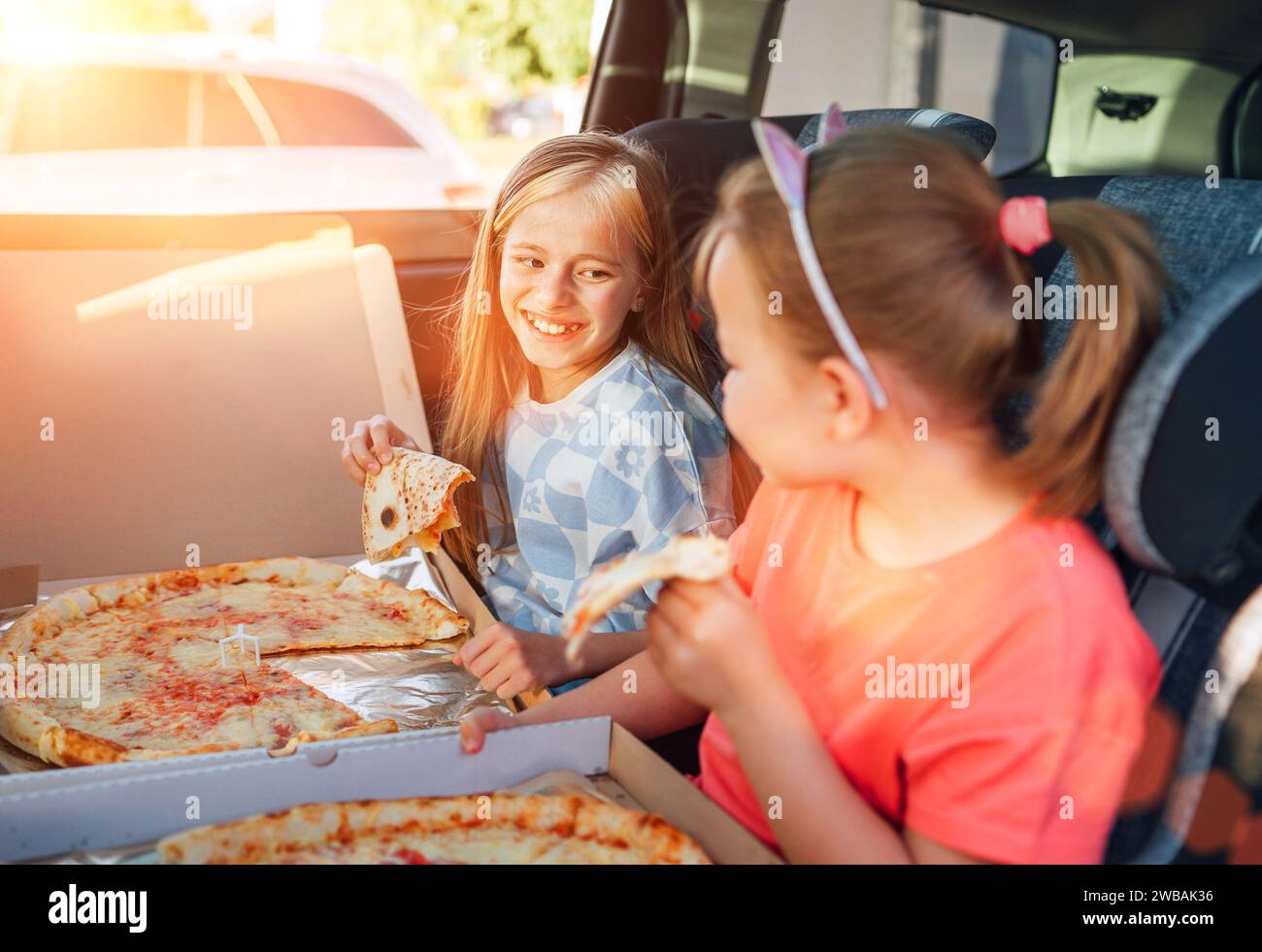 Portrait de deux sœurs souriantes et positives mangeant juste une pizza italienne cuite dans des sièges d'enfant sur le siège arrière de voiture. Bonne enfance, fastfood eatin Banque D'Images