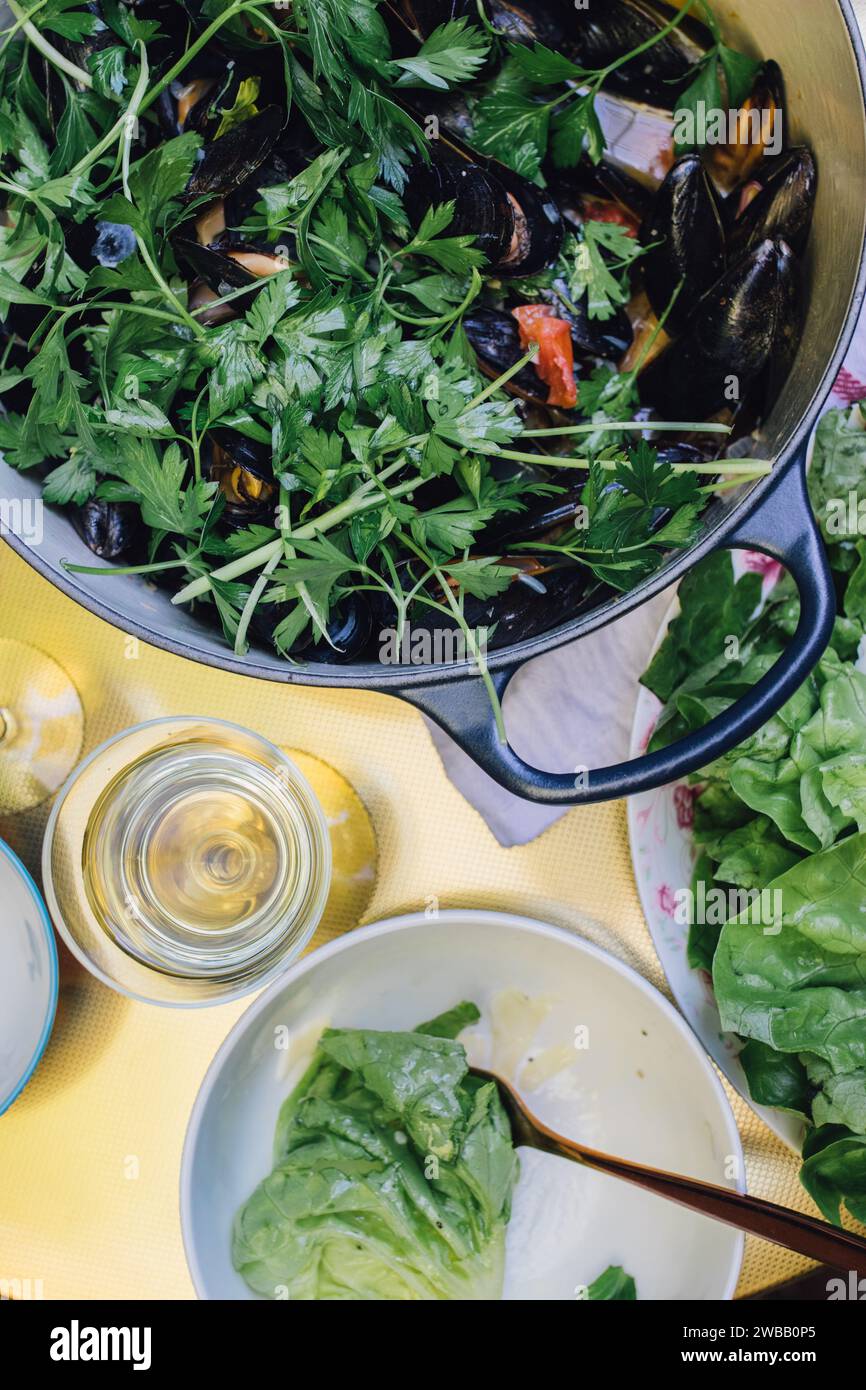 Vue grand angle de moules Mariniere sur table dorée, moules cuites à la vapeur dans une casserole avec du vin blanc, du persil italien Banque D'Images
