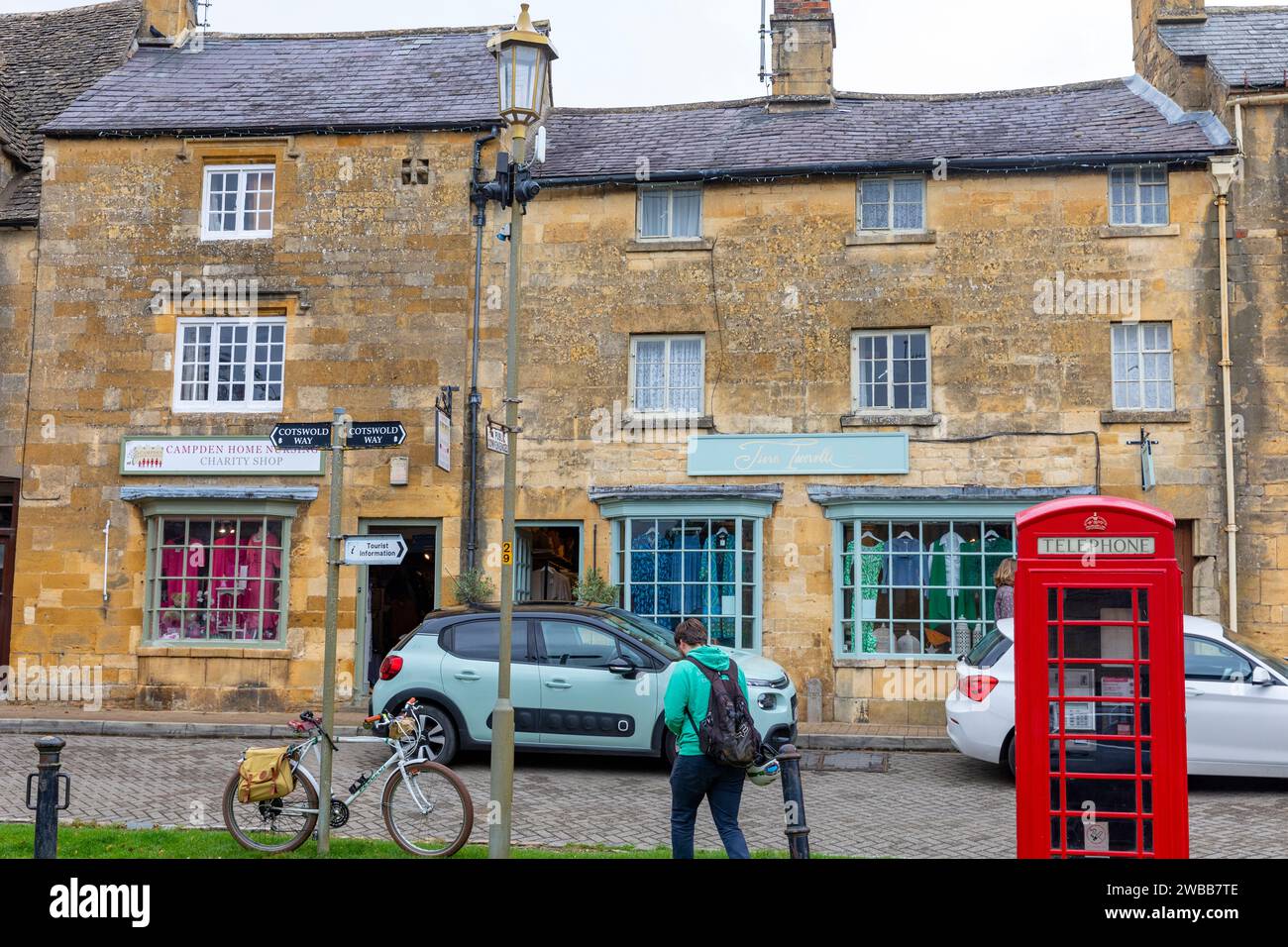 Chipping Campden, ville de marché dans les cotswolds anglais, grande rue avec boîte téléphonique rouge, bâtiments en pierre et cycliste masculin avec vélo, Angleterre, Royaume-Uni, 2023 Banque D'Images