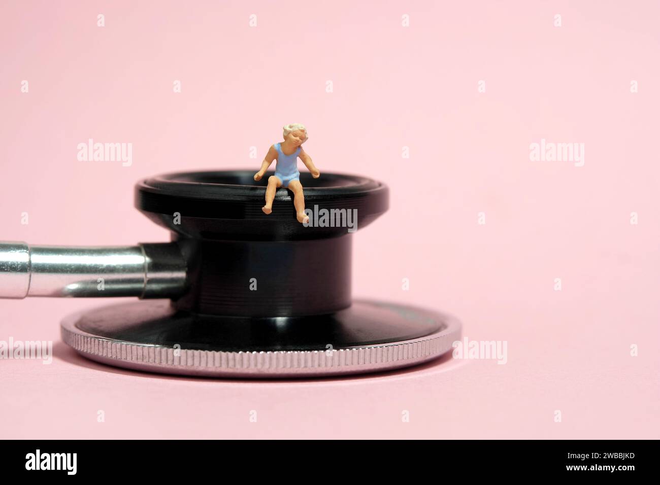 Photographie miniature de figurine de jouet de personnes minuscules. Une petite fille assise au-dessus du stéthoscope avec un ours en peluche. Isolé sur fond rose. Image photo Banque D'Images