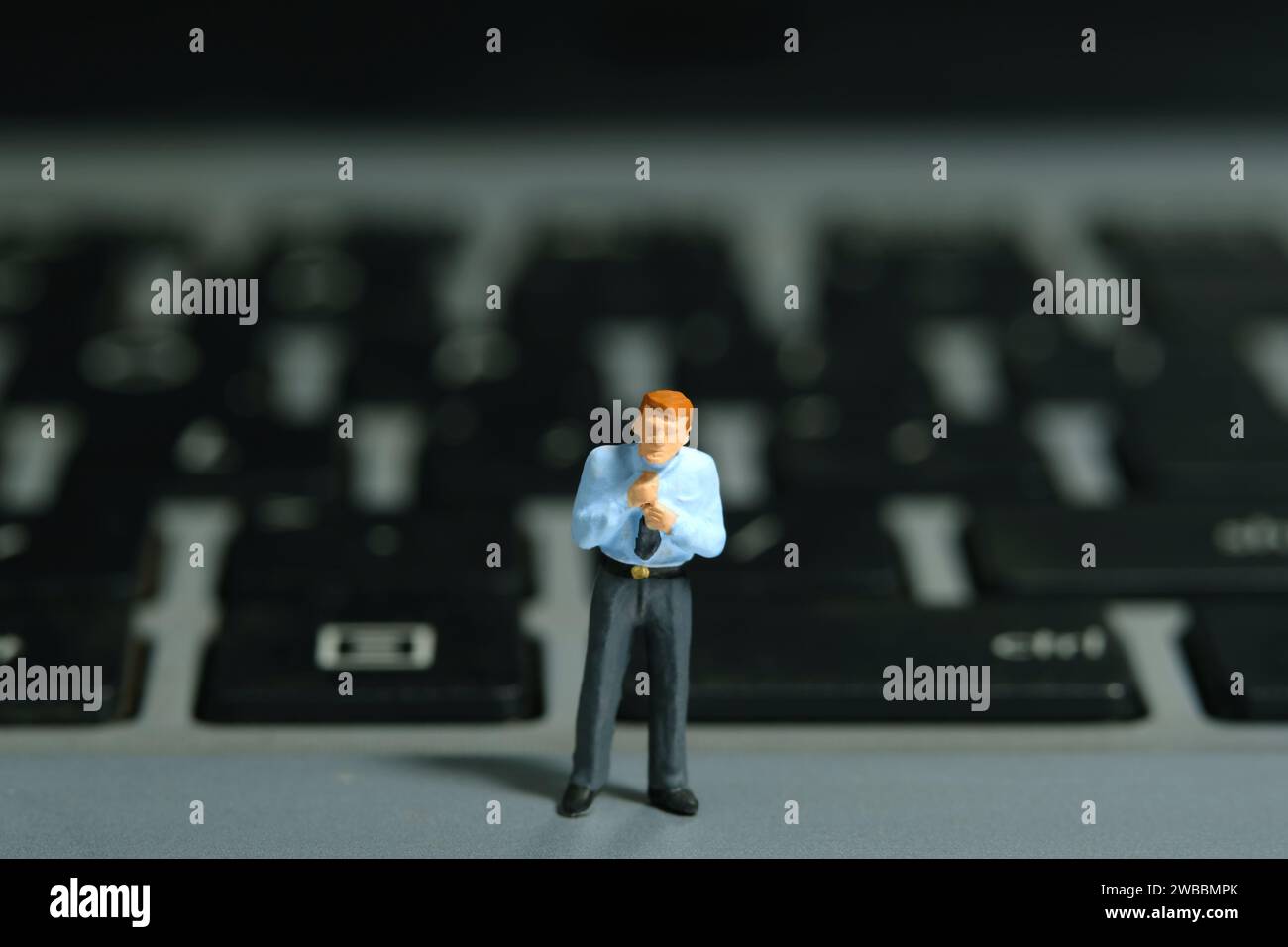 Photographie miniature de figurine de jouet de personnes minuscules. Un homme d'affaires se prépare, justifier la cravate debout au-dessus du clavier de l'ordinateur portable. Isolé sur fond blanc Banque D'Images