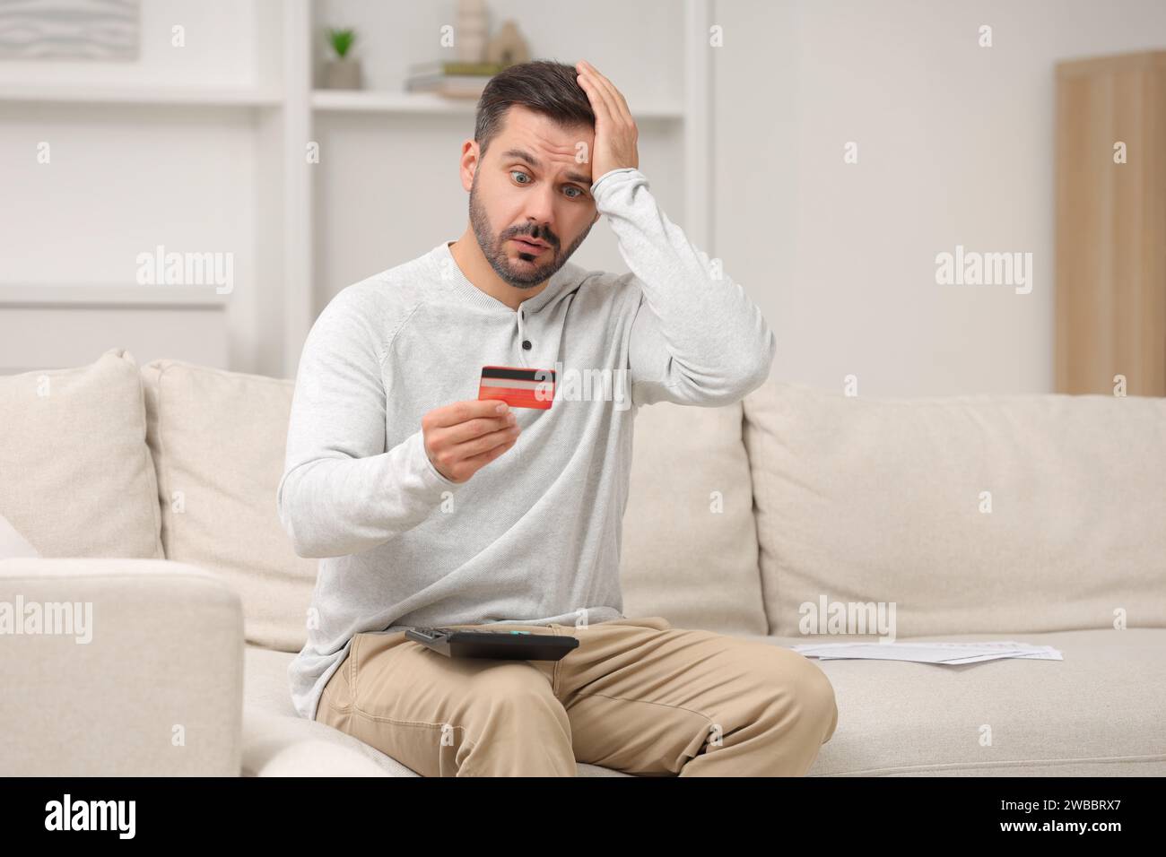 Homme choqué avec calculateur et budget de planification de carte de crédit à la maison. Problème de dette Banque D'Images