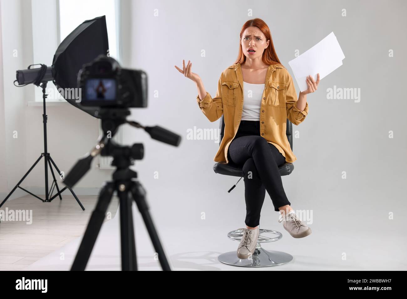 Appel de casting. Femme émotionnelle avec script jouant devant la caméra sur fond gris clair au studio Banque D'Images