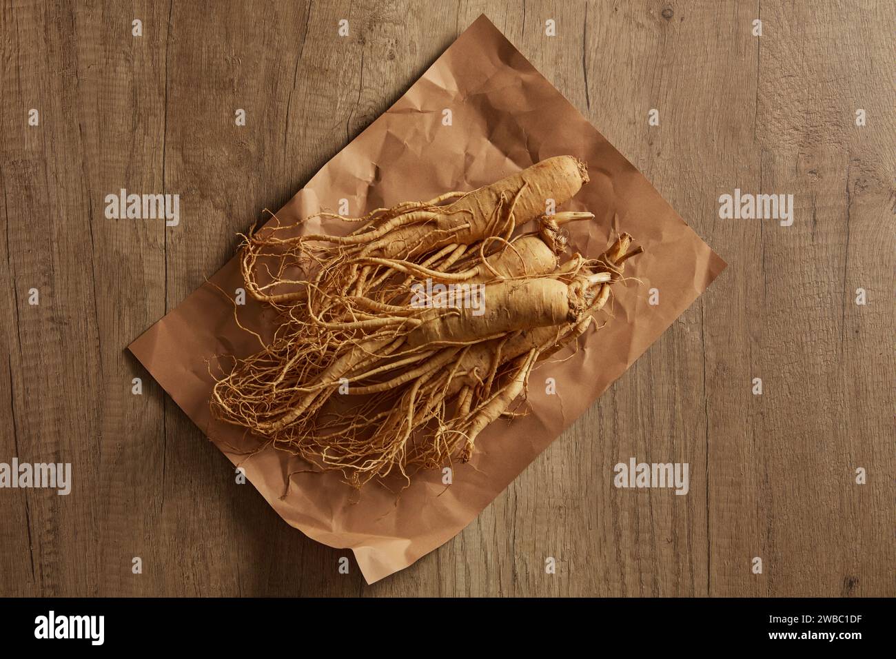 Vue de dessus, pose plate de racines de ginseng placées sur papier sur fond en bois. Gros plan de l'herbe populaire qui guérit de nombreuses maladies et est bonne pour la santé Banque D'Images