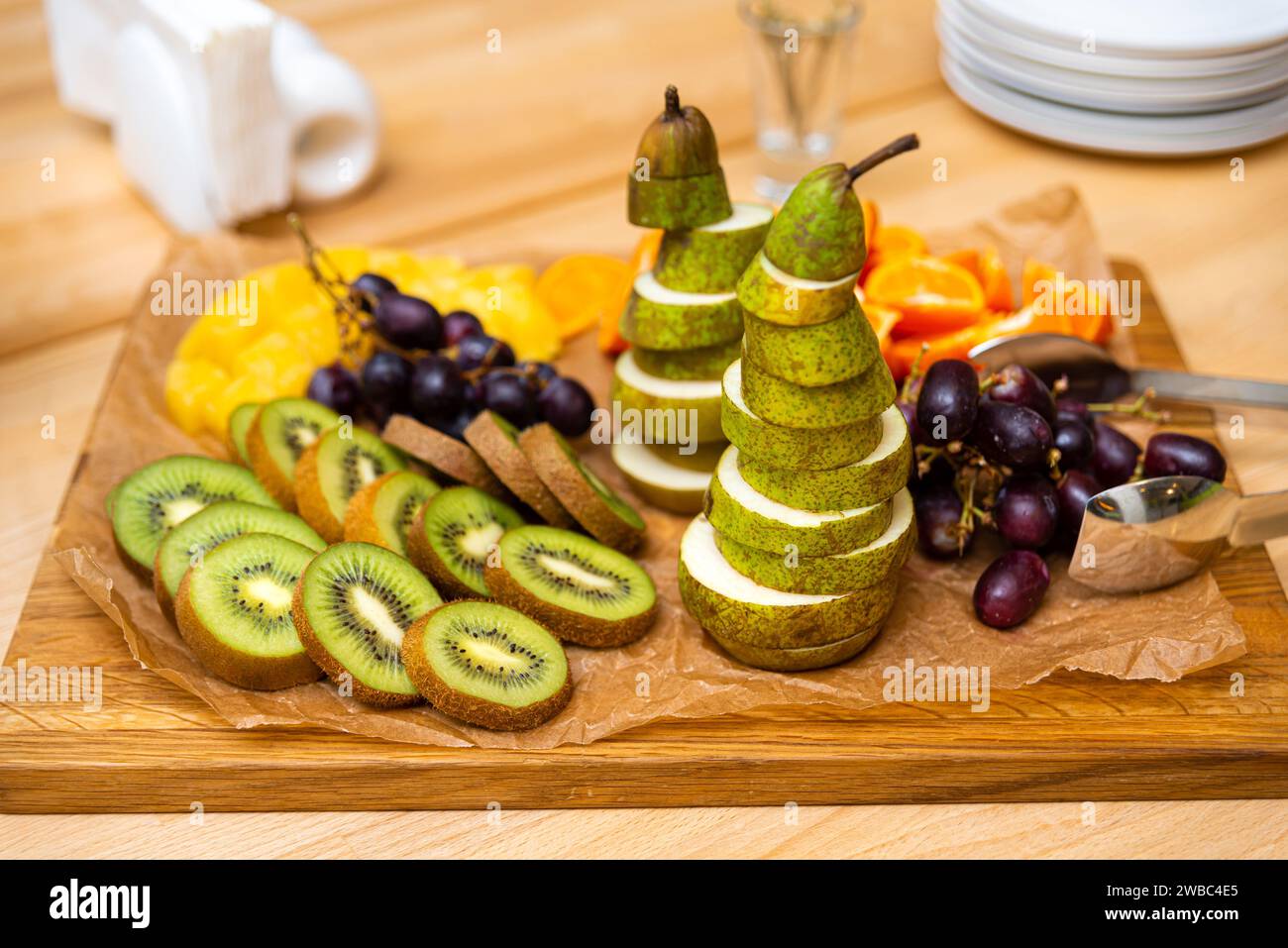 Une présentation artistique de fruits tranchés comprenant une tour de tranches de poire, kiwi et raisins, exposée sur une planche de bois pour un événement. Banque D'Images