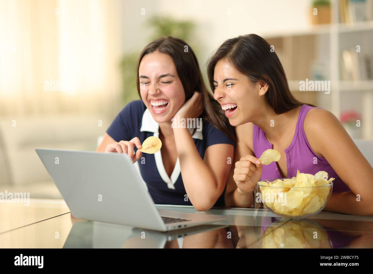 Deux amis joyeux qui regardent les médias rire et manger des chips à la maison Banque D'Images