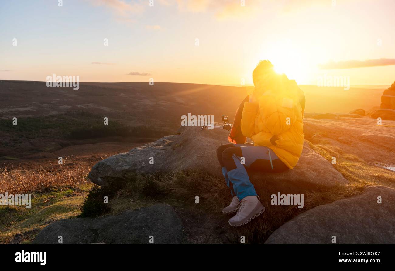 Femme en manteau jaune et écharpe orange atteignant la destination et assis sur des chaises de plage au sommet de la colline ou de la montagne au lever du soleil. Hiver froid britannique Banque D'Images