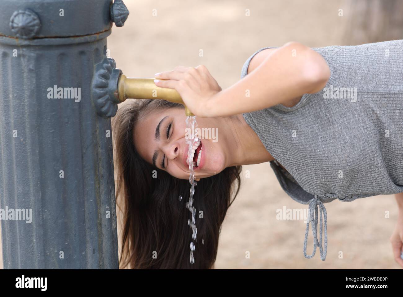 Femme heureuse riant de l'eau potable de fontaine publique dans un parc Banque D'Images