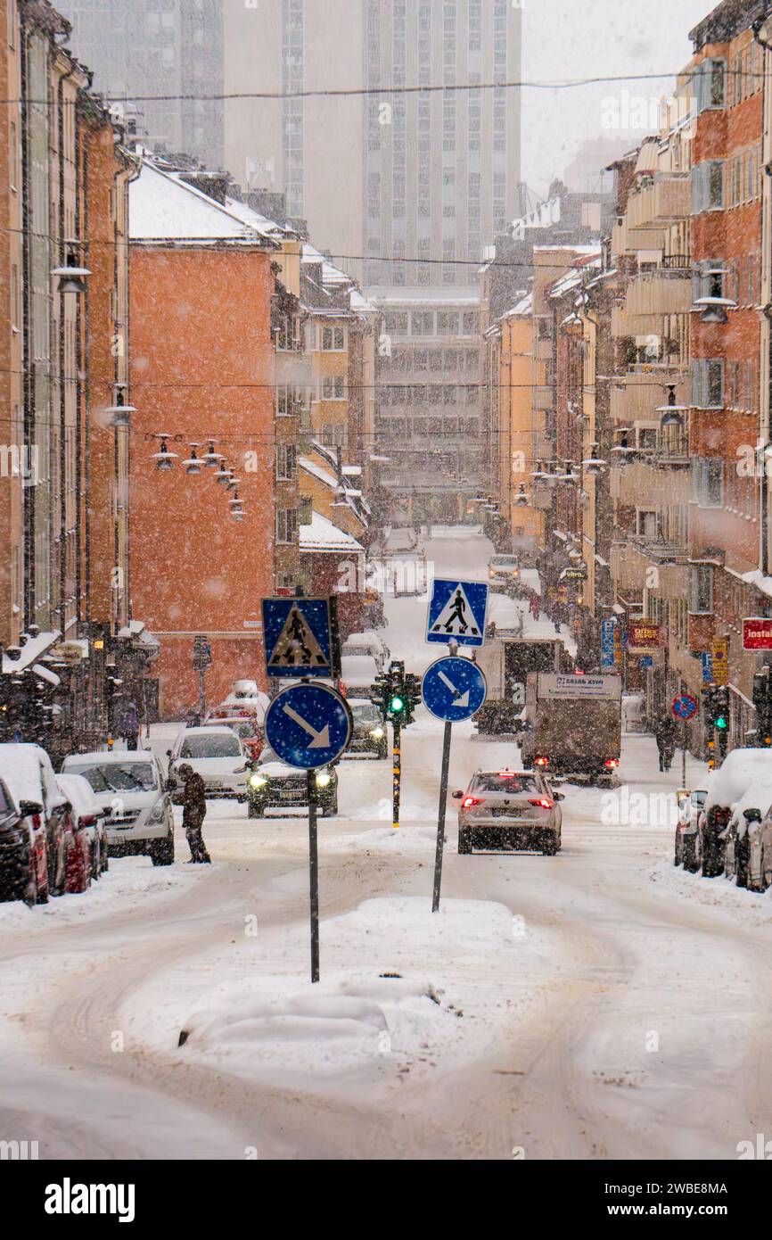 Une rue de Stockholm, Suède (Kocksgatan) pendant une tempête de neige hivernale, les gens marchent, les voitures conduisent et neige sur la route. Venteux Banque D'Images