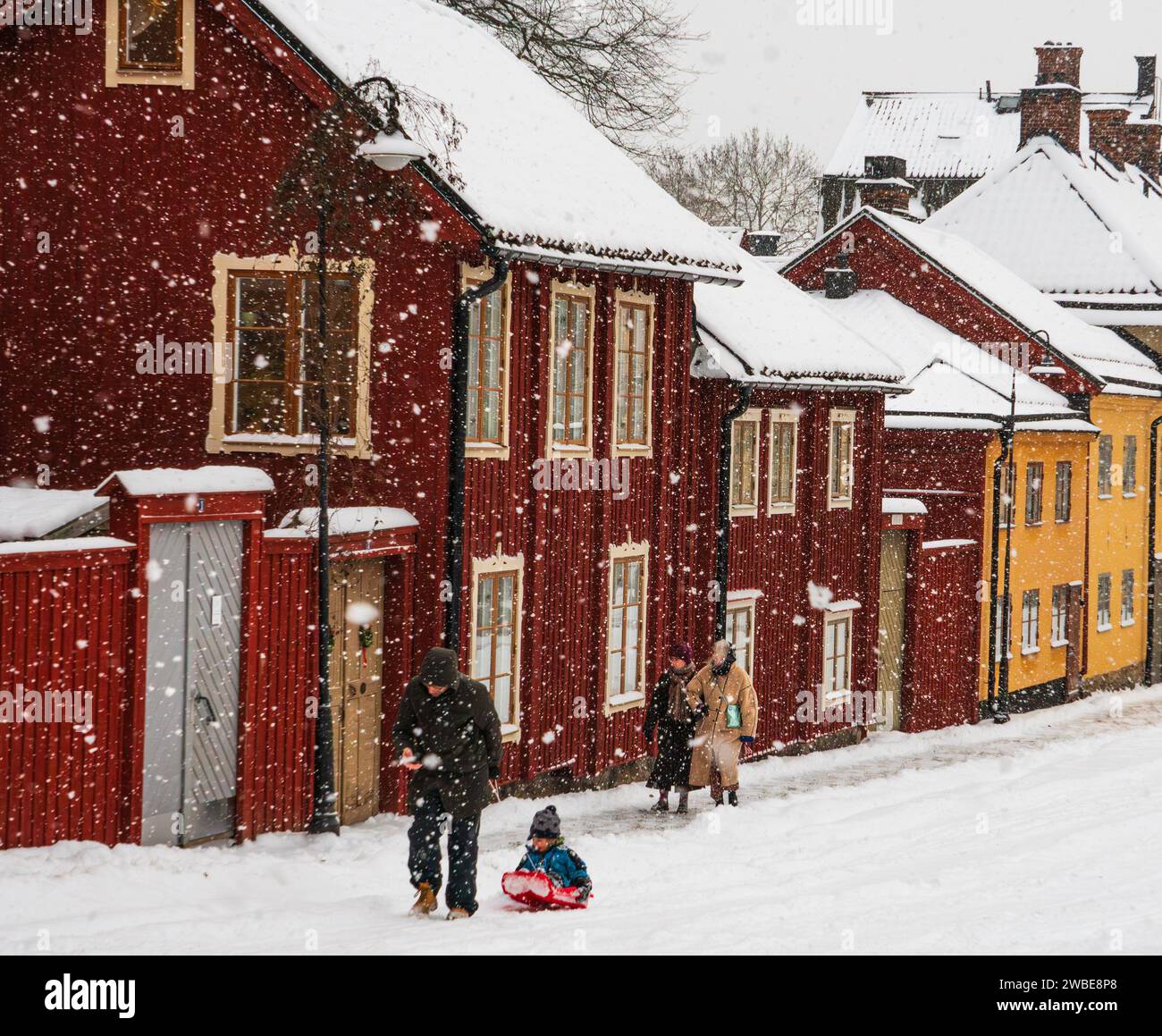 Un homme a vu traîner son enfant sur un traîneau dans le centre de Stockholm pendant une tempête de neige. Maisons historiques de couleur rouge près de la place Nytorg. Journée froide d'hiver. Banque D'Images