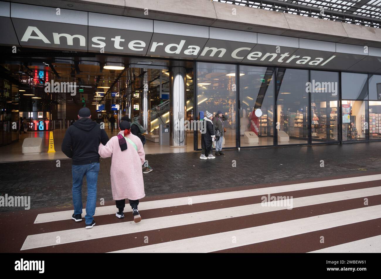 Un couple traverse la route vers la gare d'Amsterdam Centraal aux pays-Bas Banque D'Images