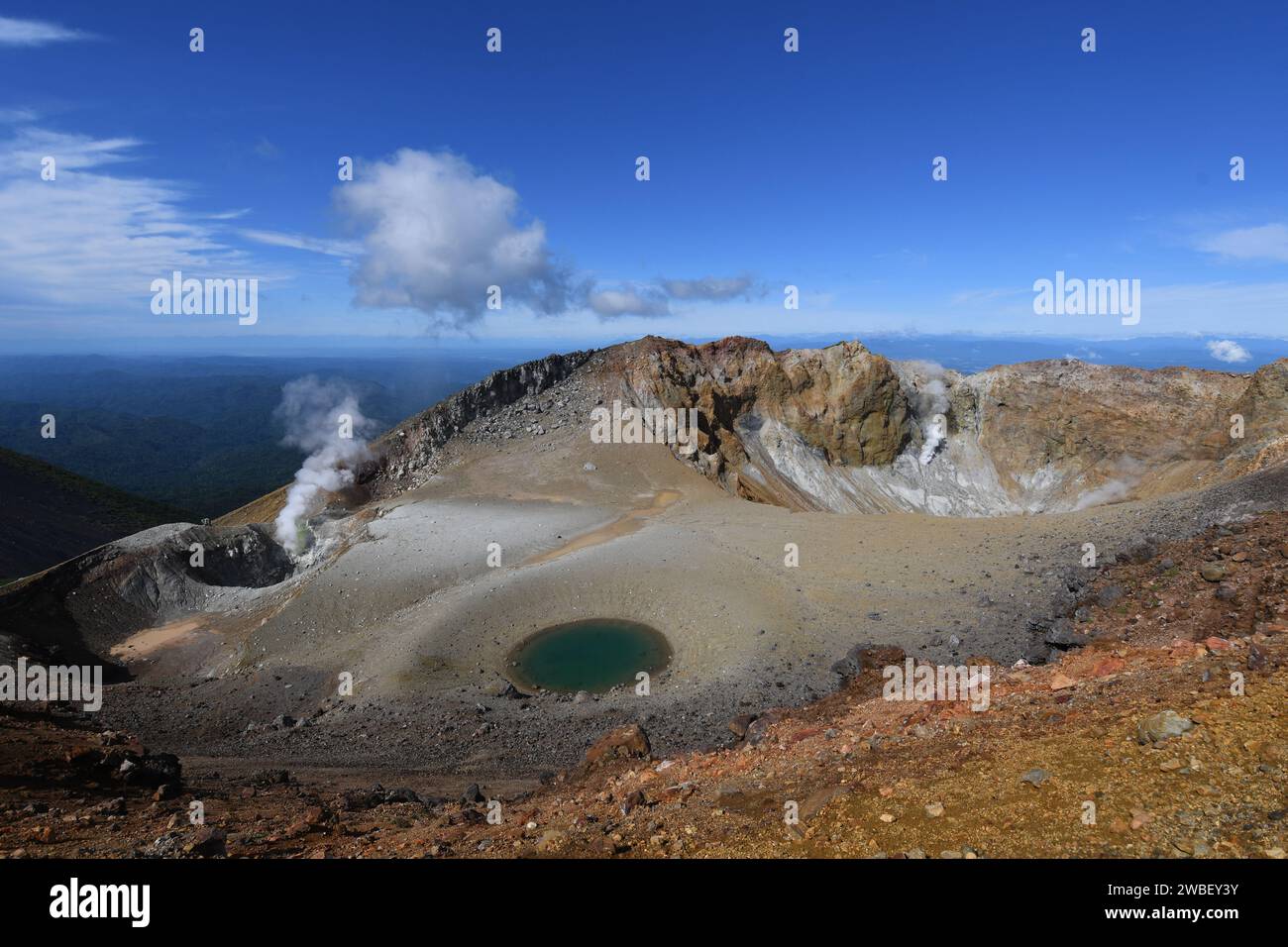 Un magnifique paysage naturel avec une source chaude nichée à flanc de montagne, entourée d'un feuillage luxuriant et d'un ciel bleu vibrant Banque D'Images