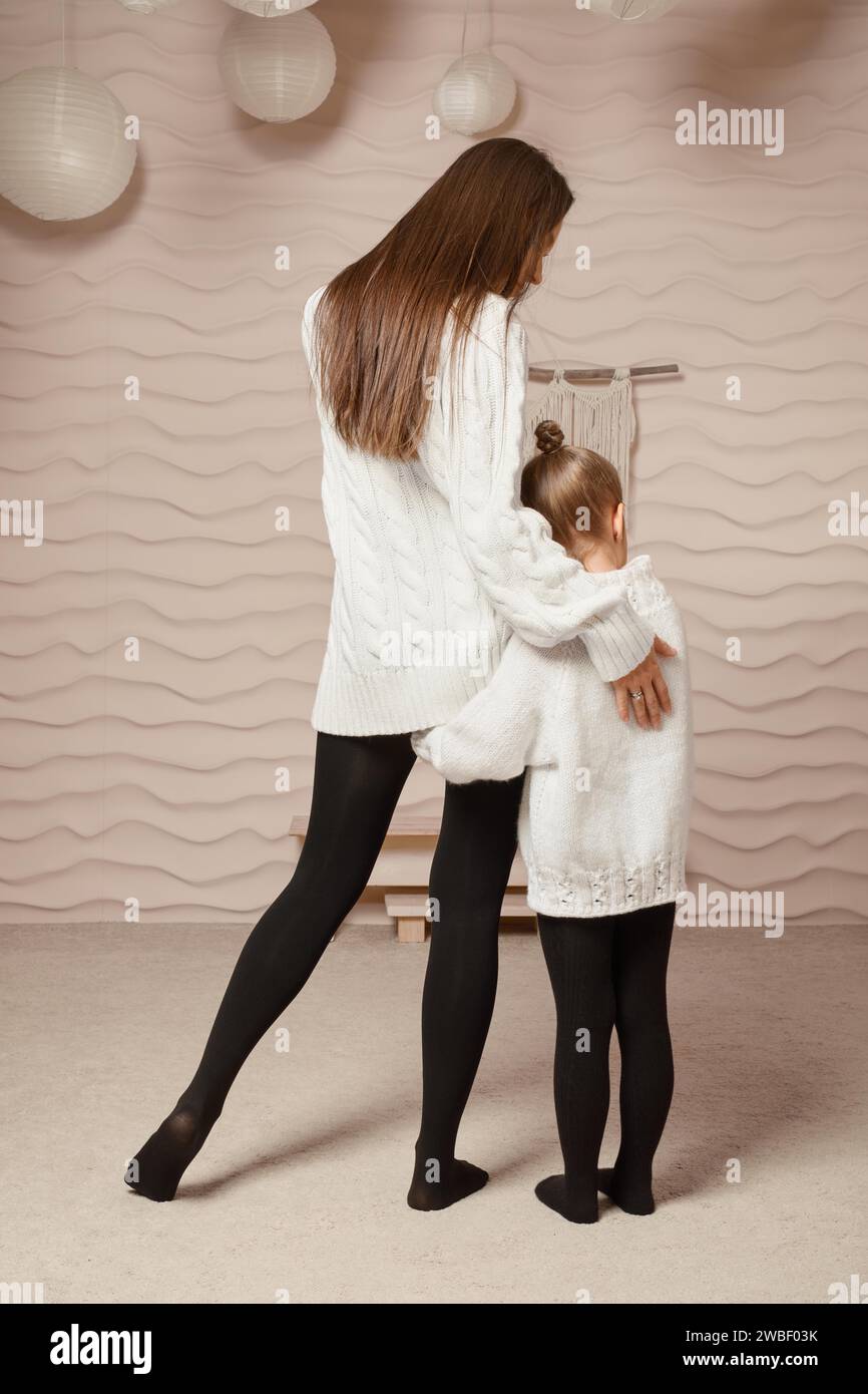 Vue arrière d'une petite fille accrochée à sa mère et serrant sa hanche Banque D'Images
