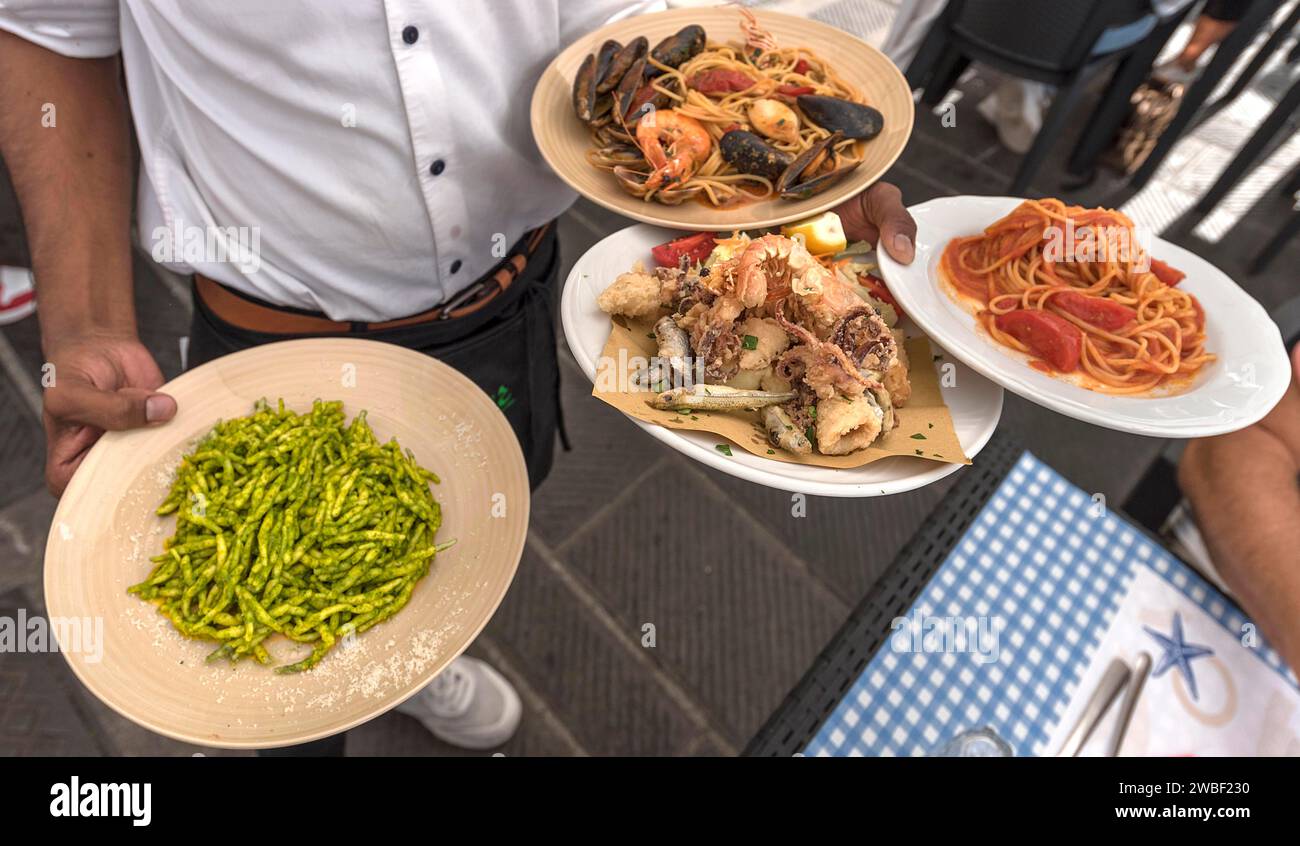 Le serveur sert trofie al pesto alla genoves, fruits de mer, spaghetti al pomodoro à une table, Gênes, Italie Banque D'Images