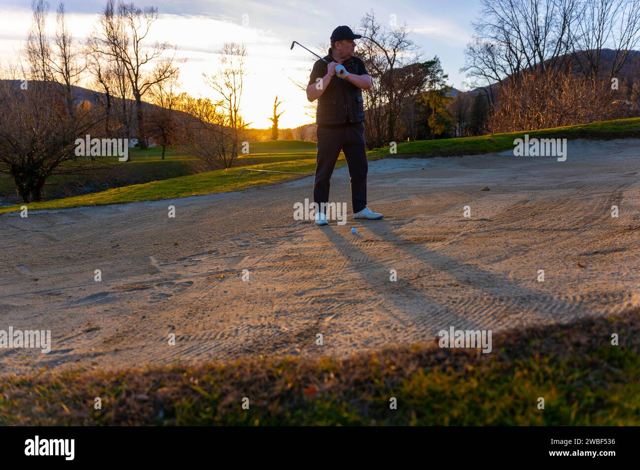 Concentration de golfeur masculin dans le piège de sable sur le terrain de golf au coucher du soleil en Suisse Banque D'Images