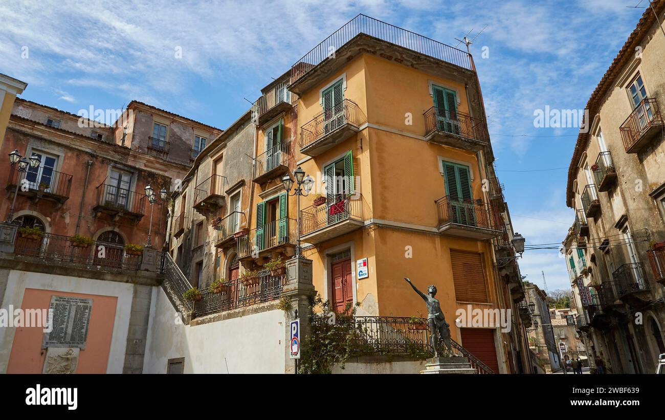 Un coin de rue dans une ville avec une statue de bronze et des balcons traditionnels, Novara di Sicilia, Sicile, Italie Banque D'Images