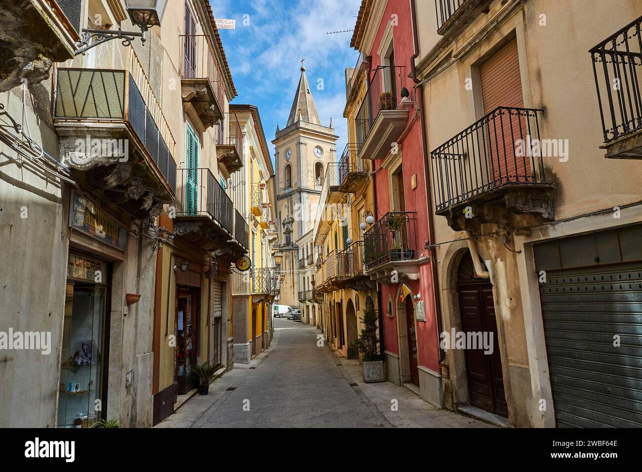 Une ruelle étroite avec des maisons colorées et une tour d'église à la fin, Novara di Sicilia, Sicile, Italie Banque D'Images