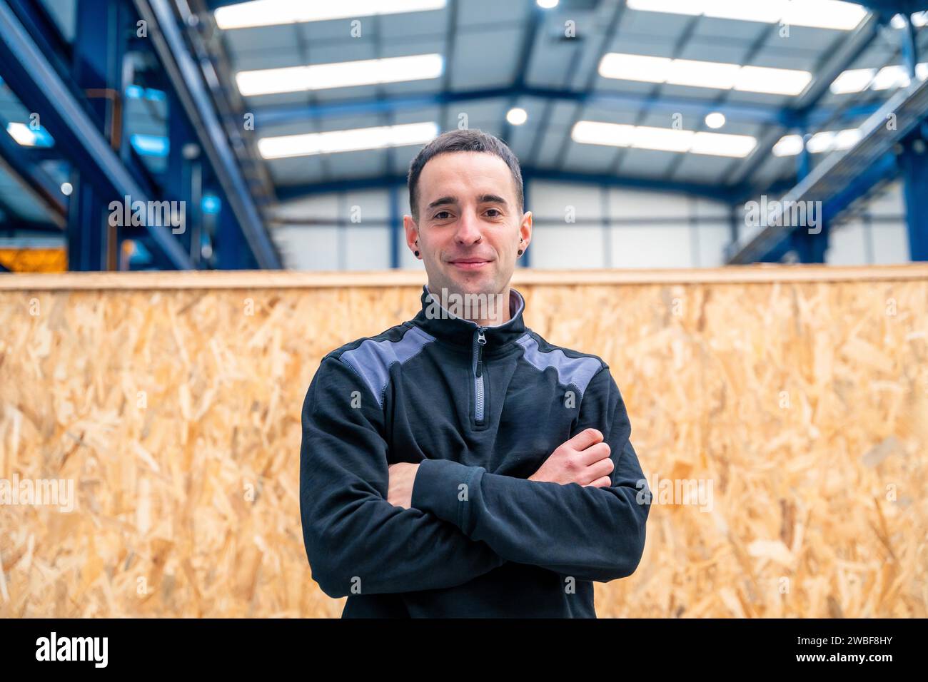 Ingénieur debout fier avec les bras croisés souriant à la caméra dans une usine Banque D'Images