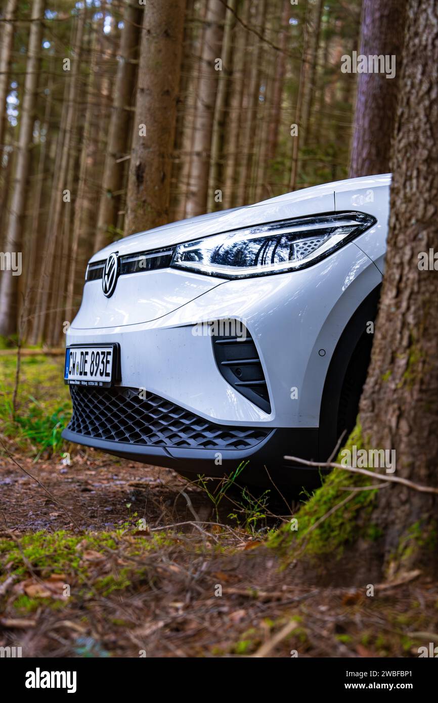 White Deer voiture électrique de Volkswagen partiellement couverte par un arbre dans la forêt, Unterhaugstett, Forêt Noire, Allemagne Banque D'Images