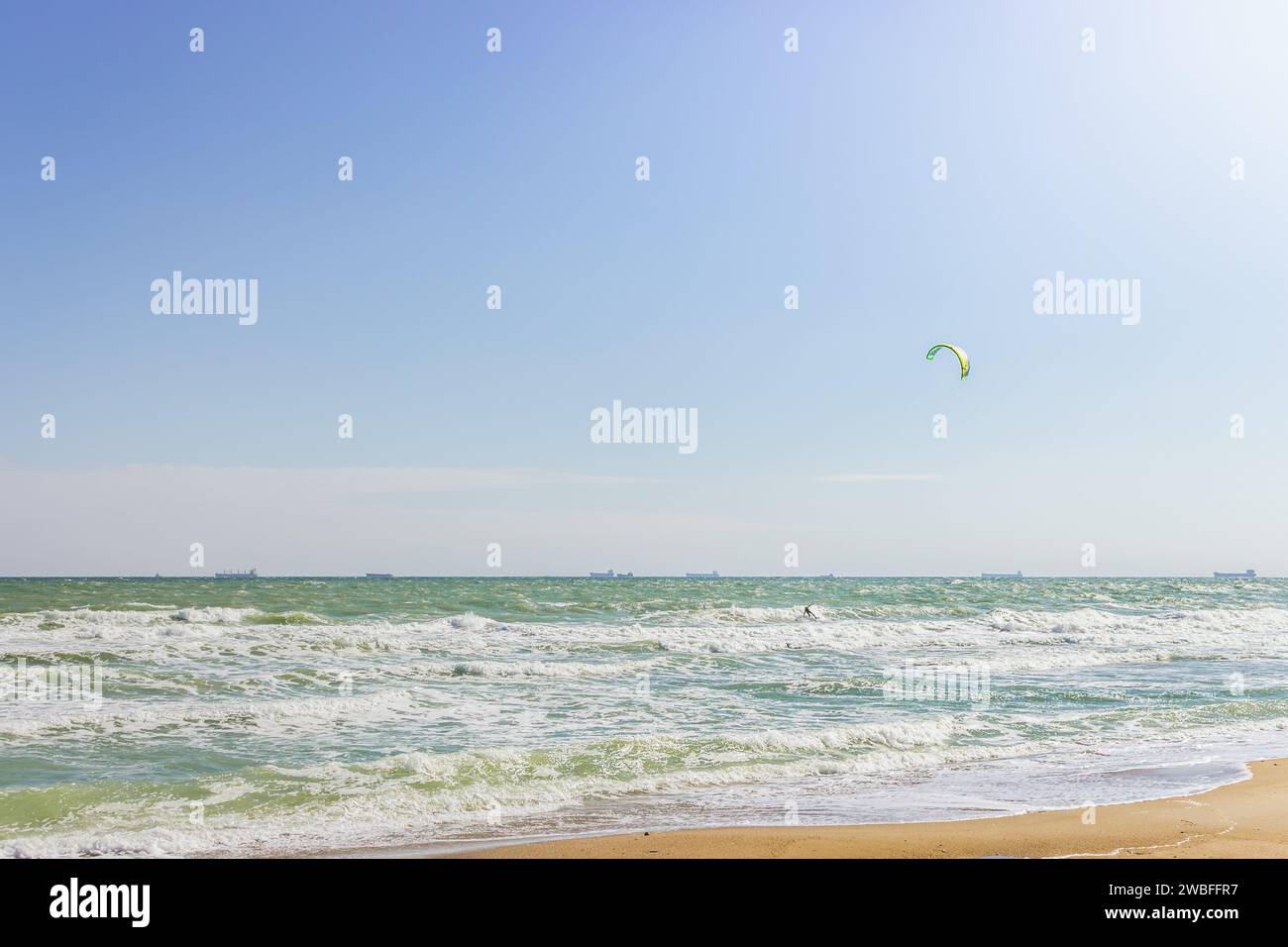Kite surf sur la plage avec des navires de commerce à l'horizon. Mode de vie actif. Concept de sports extrêmes. Homme en combinaison avec kite board au bord de la mer. Banque D'Images