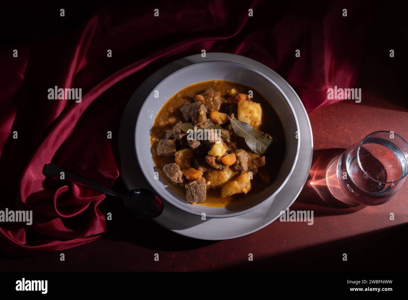 Ragoût de bœuf image conceptuelle élégante du plat méditerranéen capturé en studio à l'aide de vinyle de fond rouge avec texture, lumière dure et textile soyeux Banque D'Images