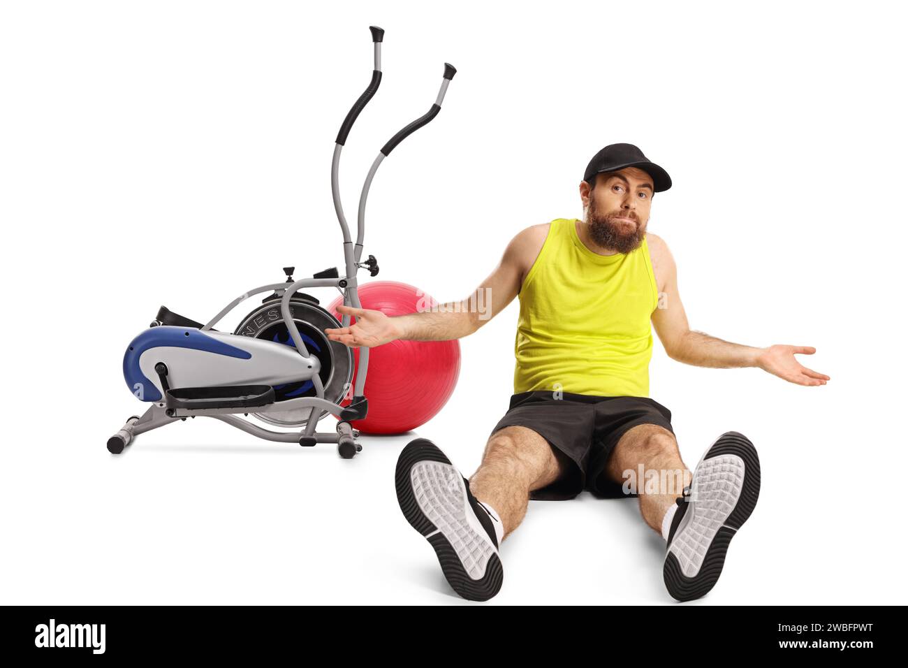 Homme barbu confus en vêtements de sport assis sur le sol devant l'équipement de gym isolé sur fond blanc Banque D'Images