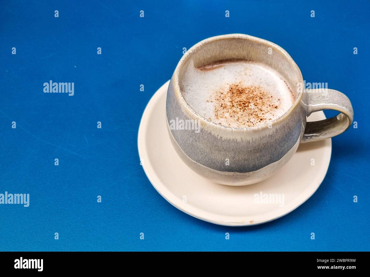 Une tasse en céramique blanche avec un liquide jaune clair et une poudre blanche sur le dessus, isolée sur un fond blanc Banque D'Images