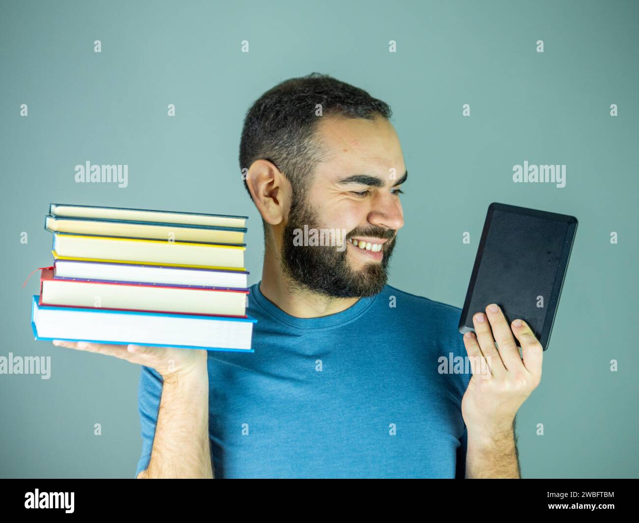 jeune homme barbu avec une pile de livres dans une main et un livre électronique dans l'autre Banque D'Images