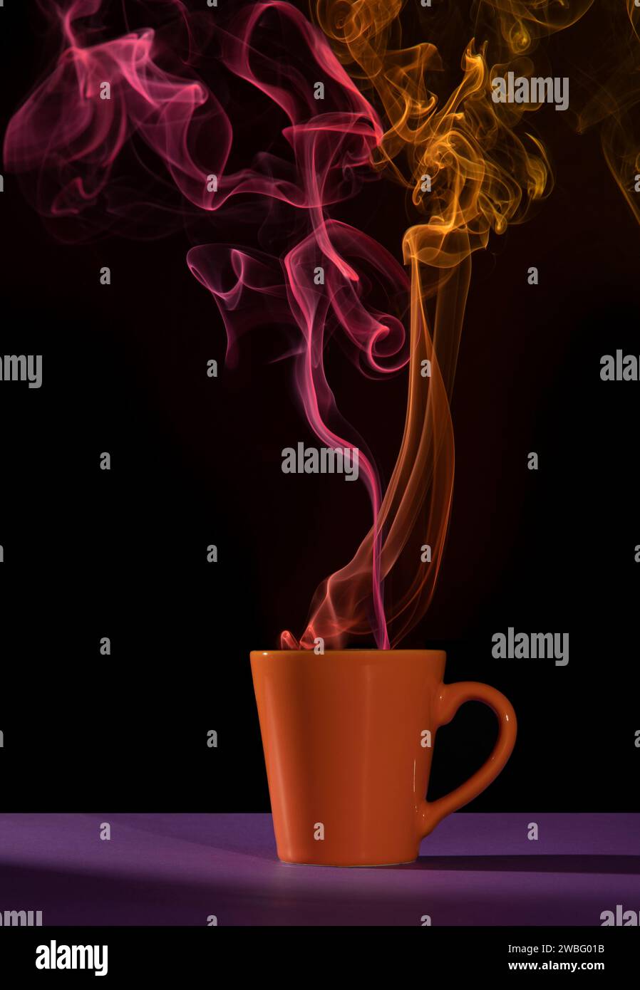 Tasse de café orange sur une table violette avec fumée rouge et jaune sur fond noir Banque D'Images