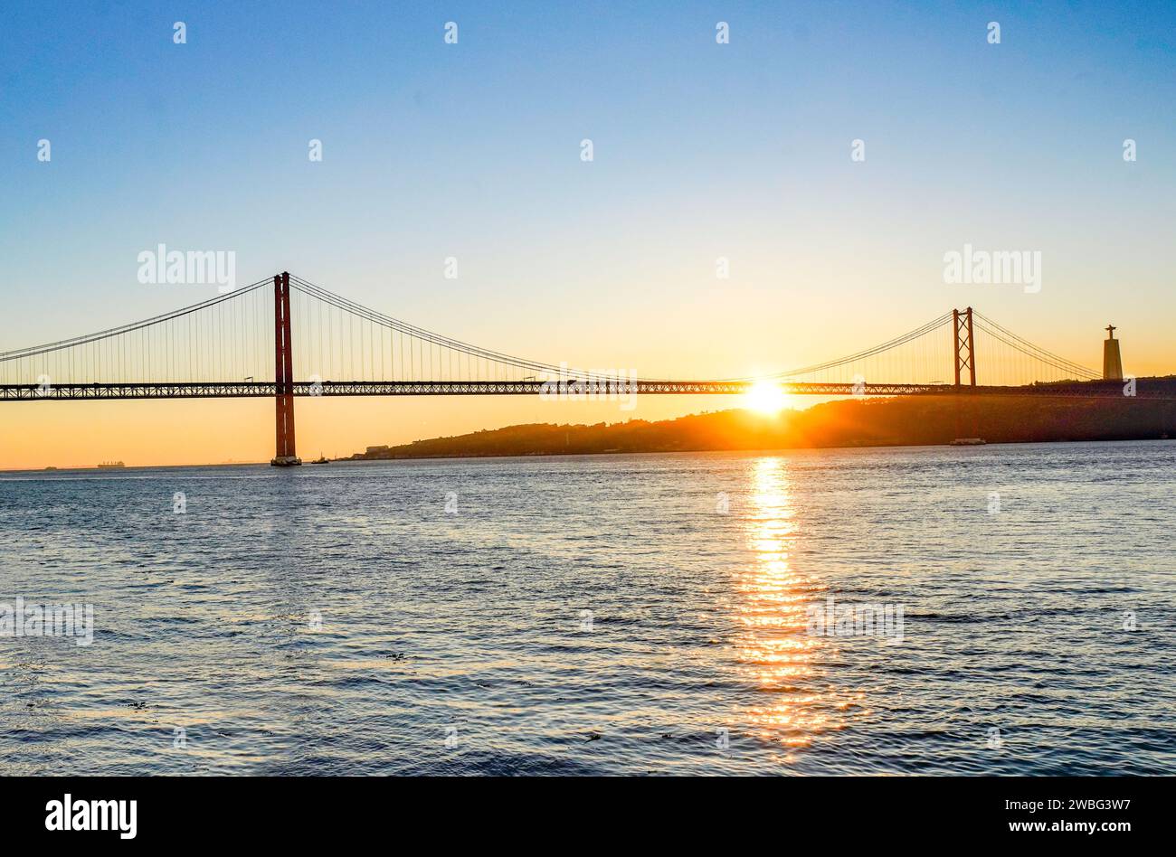 Lever de soleil doré derrière le pont 25 de Abril à Lisbonne, Portugal, projetant une lueur chaude sur le Tage dans un moment de paix et de beauté. Banque D'Images