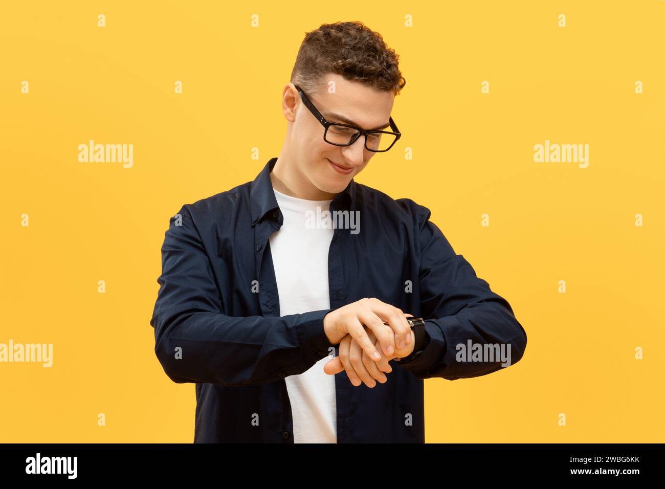 Jeune homme positif dans les lunettes vérifiant le temps Banque D'Images