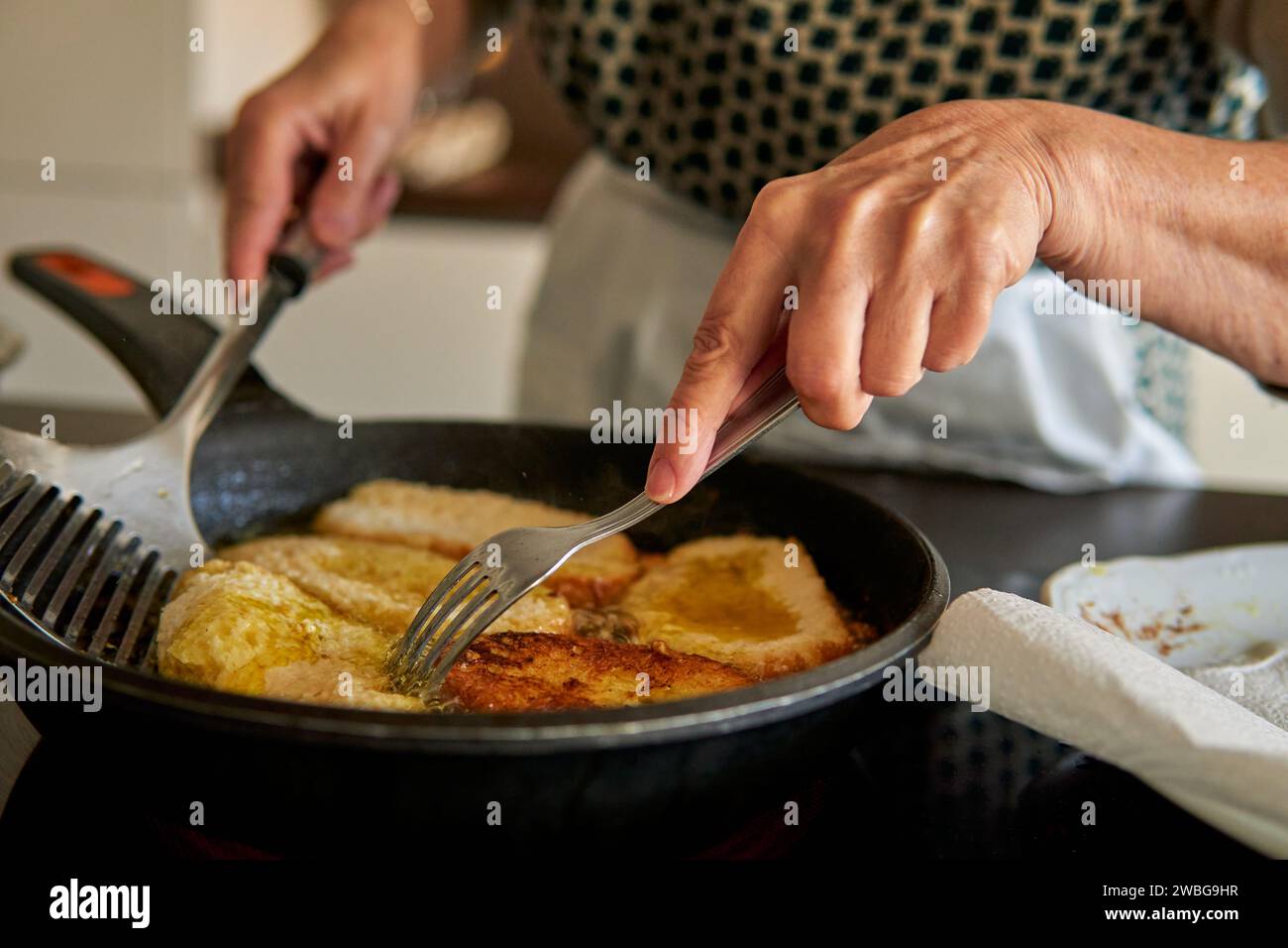 Gros plan sur les mains d'une femme âgée qui fait frire des toasts latino-français. Faire une recette traditionnelle sur une cuisinière électrique contemporaine Banque D'Images