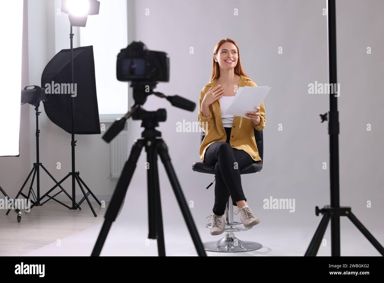 Appel de casting. Femme avec script jouant devant la caméra sur fond gris clair au studio Banque D'Images