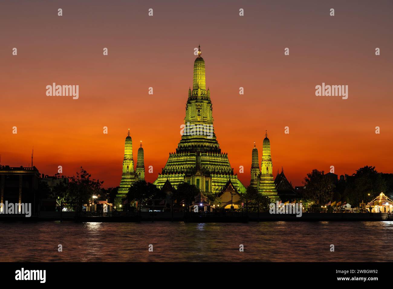 Wat Arun (Temple de l'aube) à Bangkok au crépuscule. Temple et prangs baignés de lumière jaune. Approfondissement du ciel orange en arrière-plan. Rivière Chao Phraya. Banque D'Images