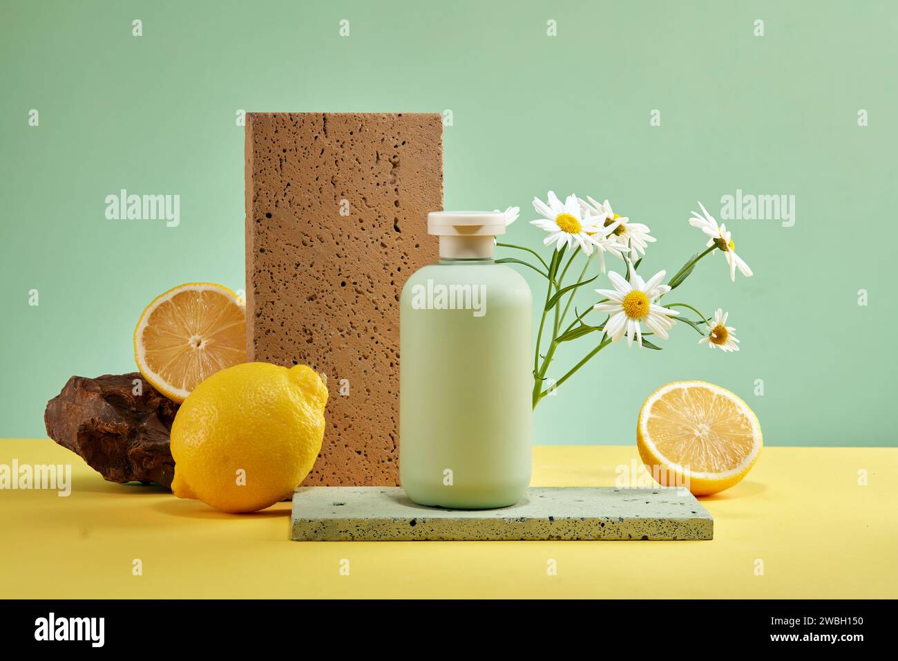 Une bouteille vide sans étiquette placée sur un podium en brique décoré de citron frais, de roche et de fleur blanche sur fond vert. Scène de maquette pour adverti Banque D'Images