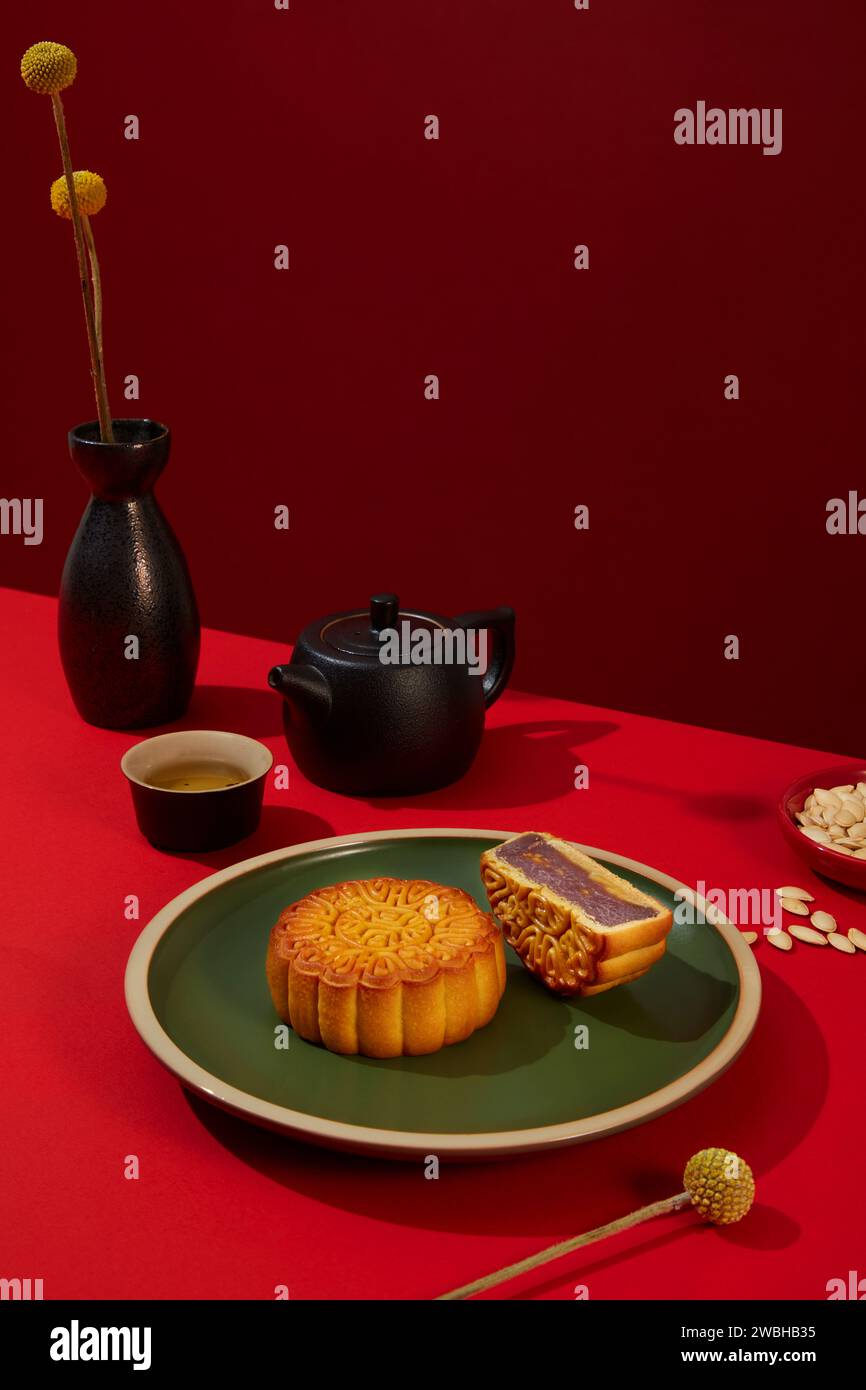 Plat en céramique verte avec un gâteau de lune complet et une moitié de gâteau de lune placé sur. Pot de fleurs noires et service à thé arrangé. Les gens mangent souvent un repas de réunion pendant Banque D'Images