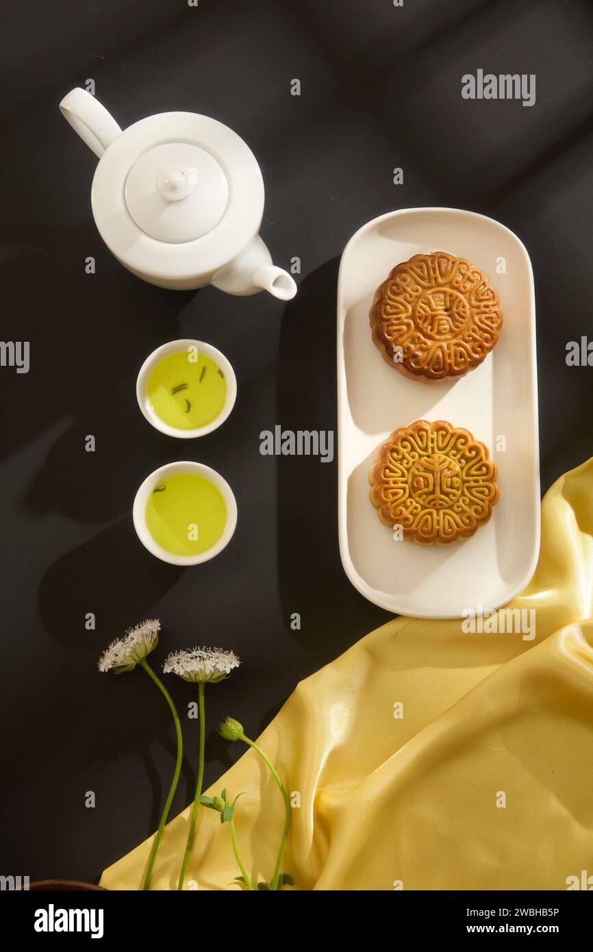 Un ensemble de thé décoré de deux délicieux gâteaux de lune placés sur un plat en céramique. Tissu jaune avec des fleurs en vedette. Fête de la mi-automne traditi chinois Banque D'Images
