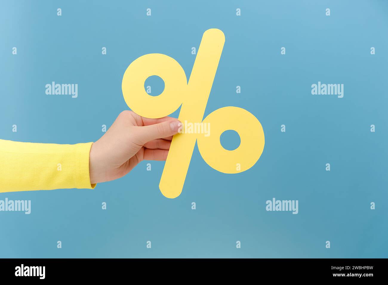 Gros plan de la main de femme tenant la marque de pourcentage jaune de papier, présentant de grandes réductions, posant isolé sur le mur de fond bleu Uni dans le studio wi Banque D'Images