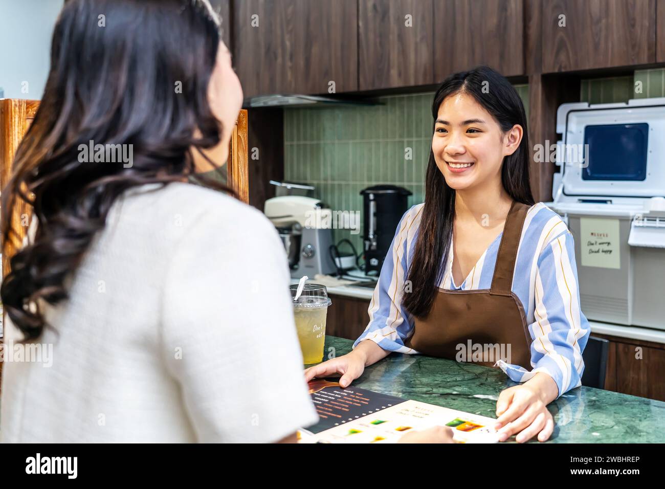 Jeune serveuse asiatique souriante dans un café avec le client pour le service, le paiement ou la commande sur le comptoir au café. Banque D'Images
