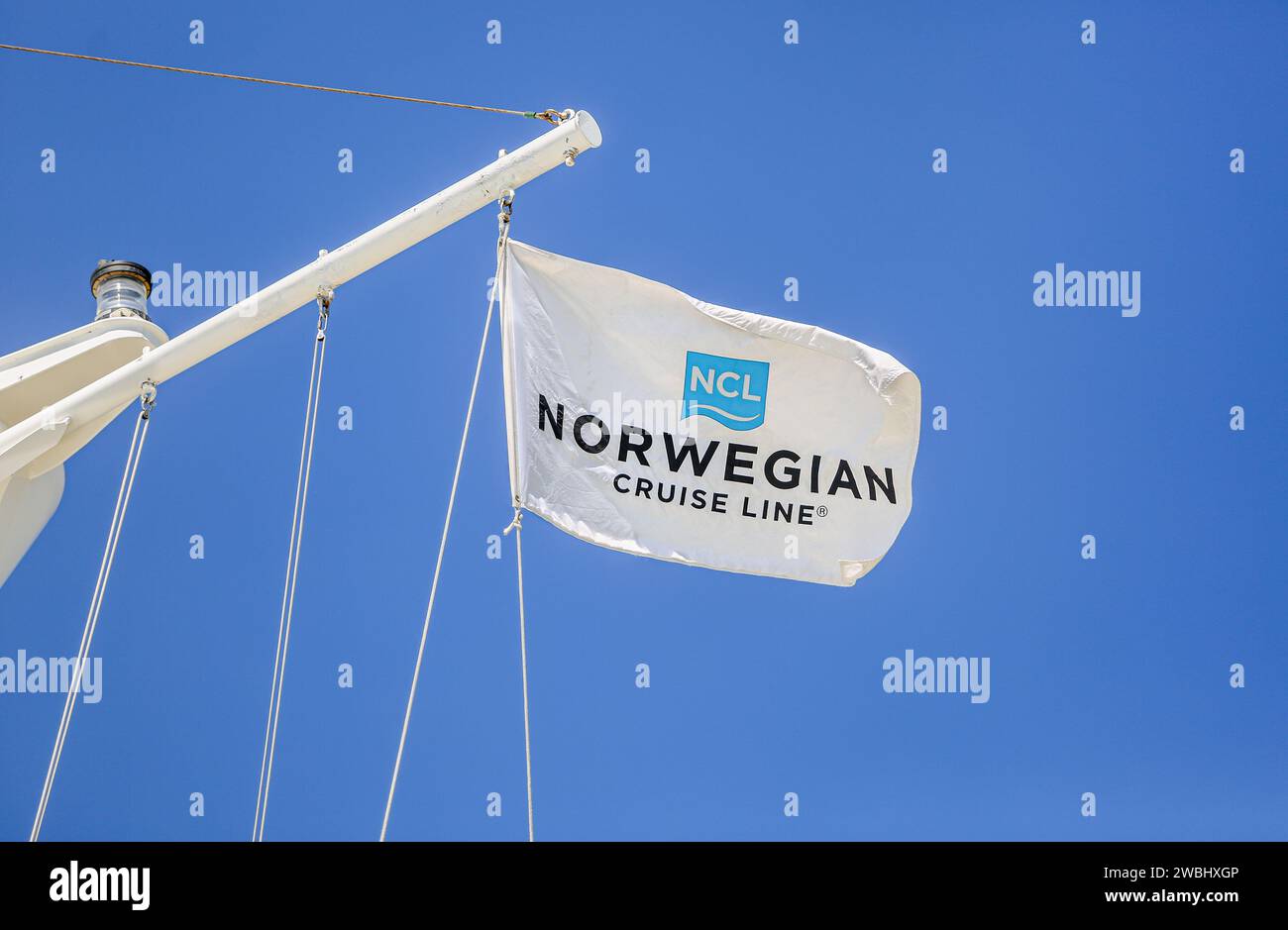 Norwegian Cruise Line logo flag (NCL), le drapeau de la compagnie de croisières basée à Miami vole sur un mât de navire de croisière avec feu de navigation, fond de ciel bleu Banque D'Images