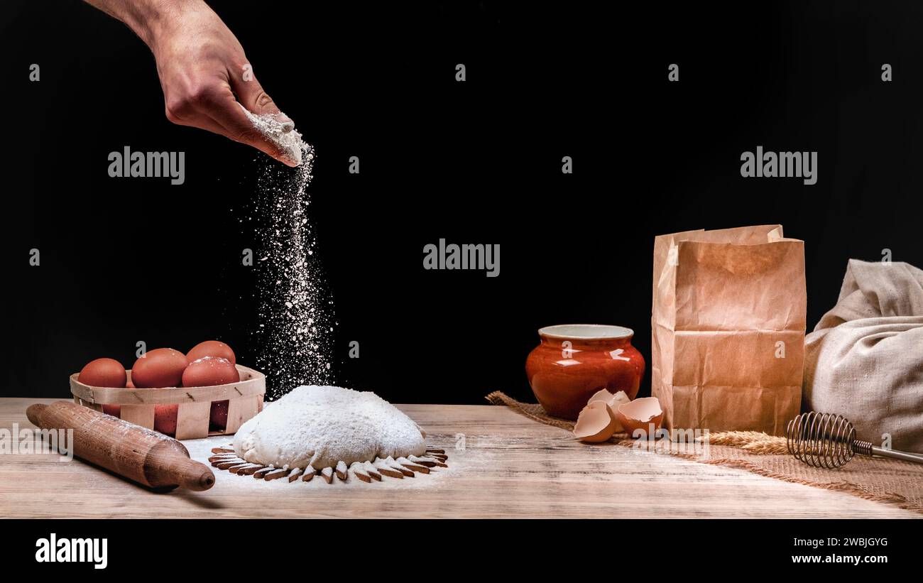 La main des boulangers dort la pâte avec de la farine. Cuisson du pain. La pâte repose sur une table de cuisine en bois et saupoudrée de farine sur le dessus. Banque D'Images