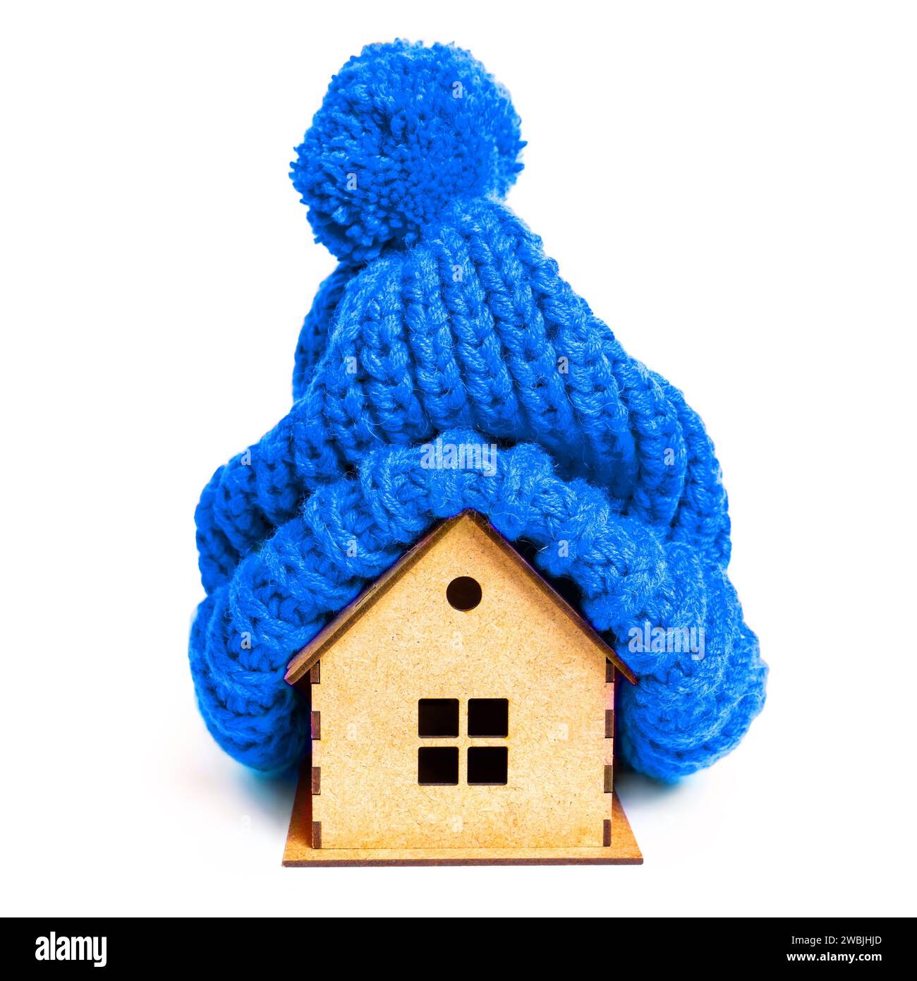 Minuscule maison en bois ornée d'un élégant bonnet en tricot bleu isolé sur blanc. Concept lié à l'isolation créative de la maison et aux préparations saisonnières. Banque D'Images