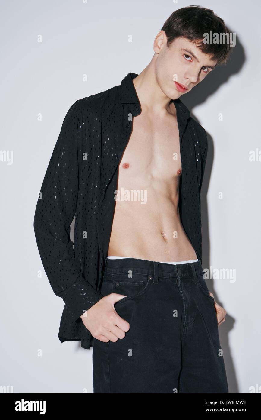jeune homme confiant en chemise ouverte noire brillante avec le doigt dans la poche de pantalon sur fond gris Banque D'Images